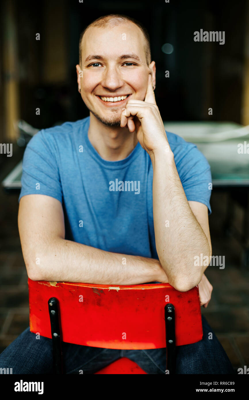 Happily smiling caucasian man in blue shirt sitting on a red chair Stock Photo