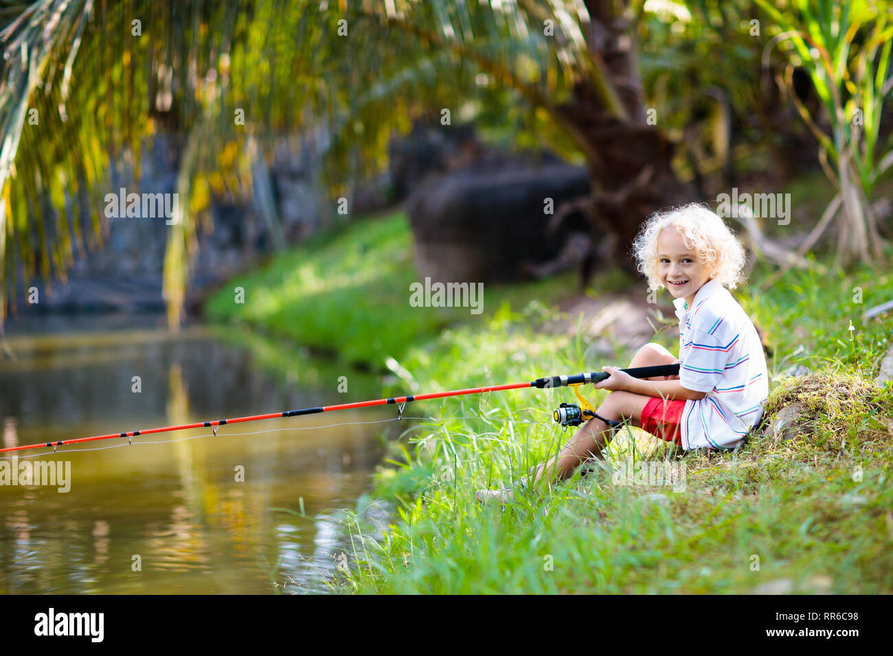 Boy fishing. Child with red rod catching fish in river on sunny