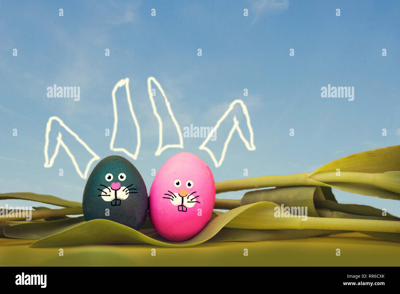 painted Easter eggs with bunny face and blue sky, lying in tulips, easter spring concept Stock Photo