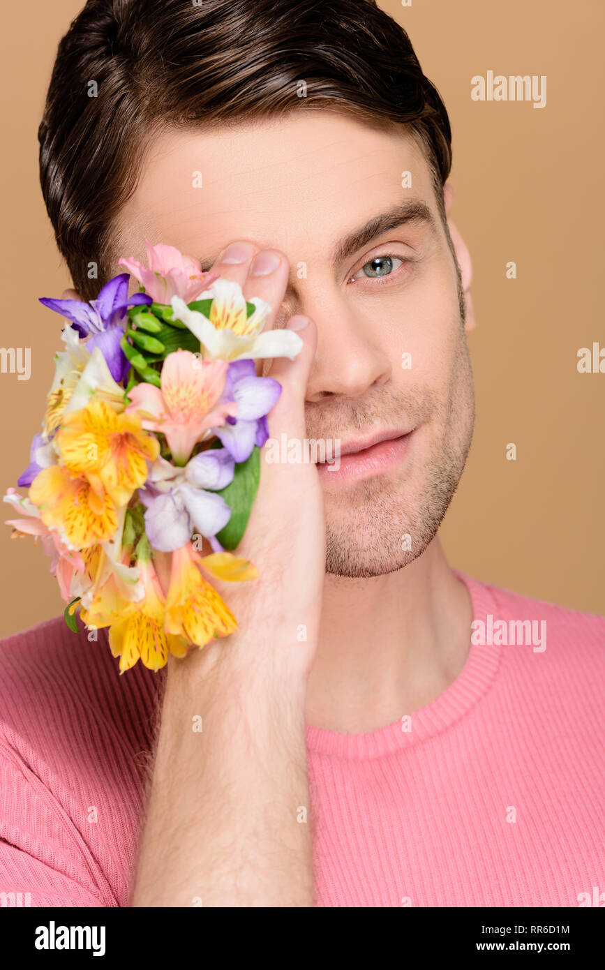 handsome man covering one eye with flowers on hand isolated on beige Stock Photo