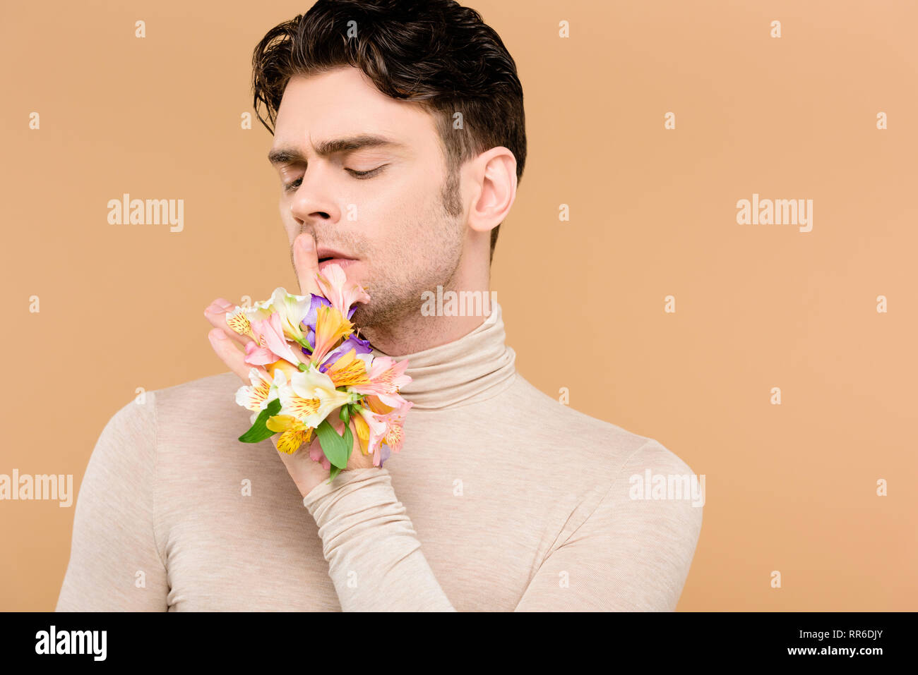 man with alstroemeria flowers on hand showing hush sign isolated on beige Stock Photo