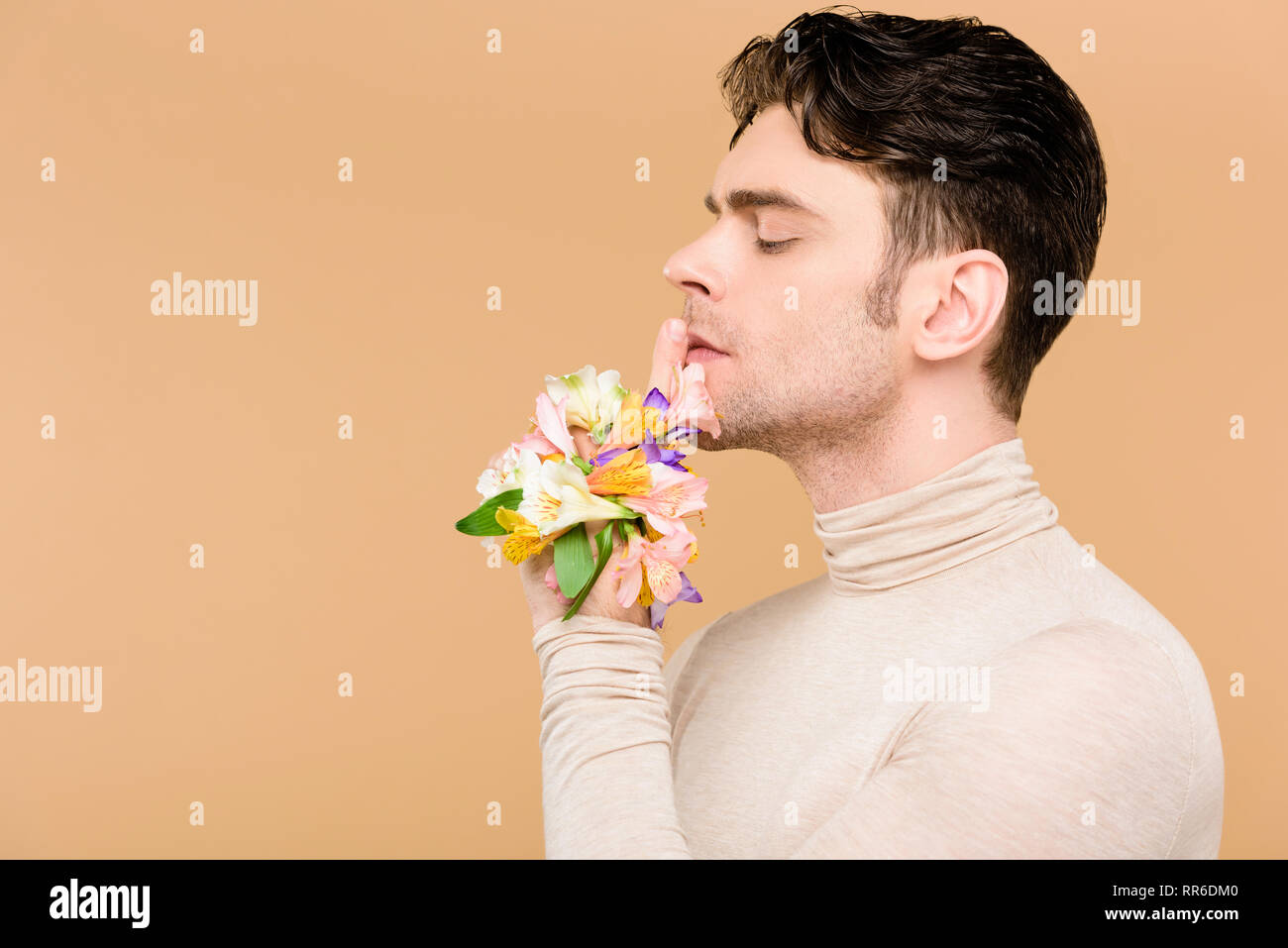 profile of handsome man with alstroemeria flowers on hand showing hush sign isolated on beige Stock Photo