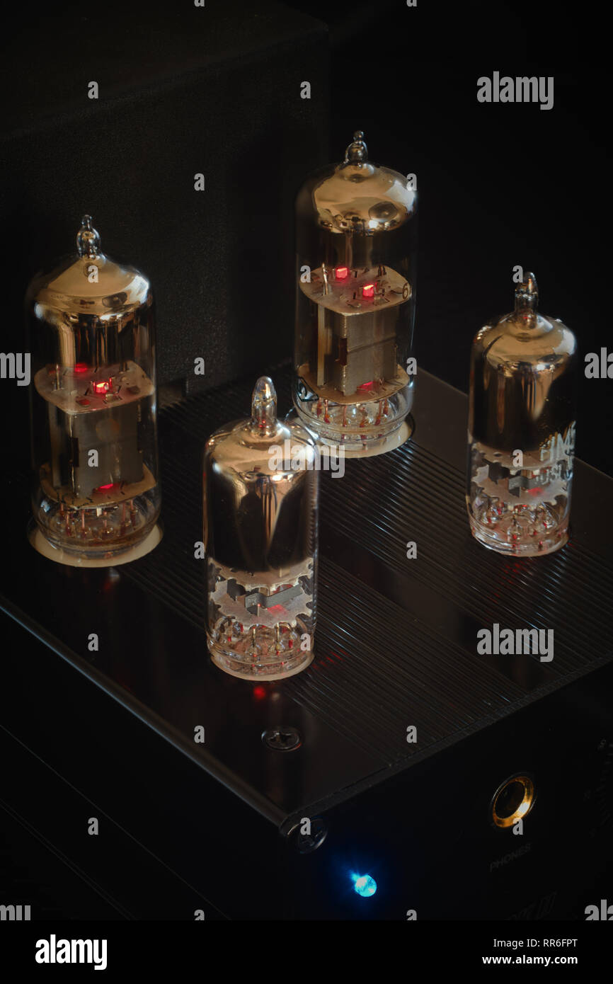 Headphone amplifier with four glowing vacuum tubes / valves against a black background. Vertical / portrait aspect. Stock Photo