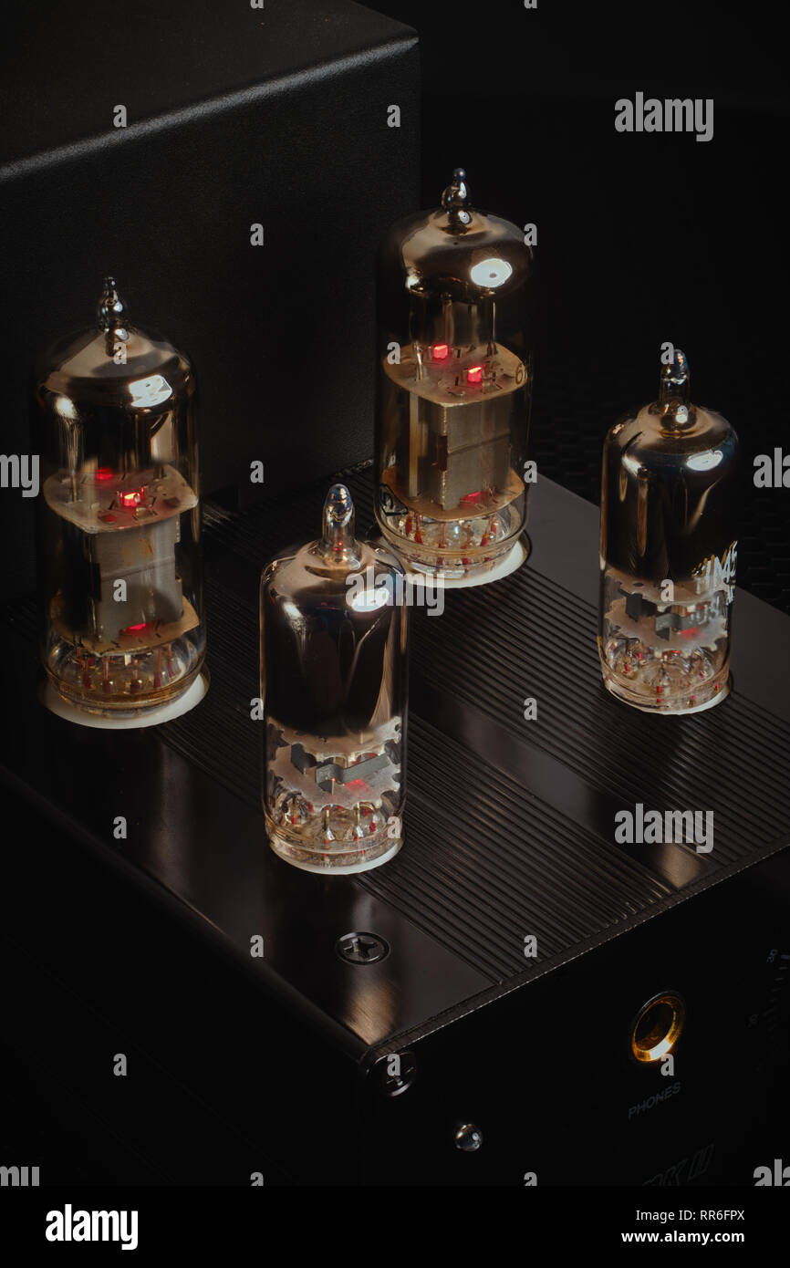 Headphone amplifier with four glowing vacuum tubes / valves against a black background. Vertical / portrait aspect. Stock Photo