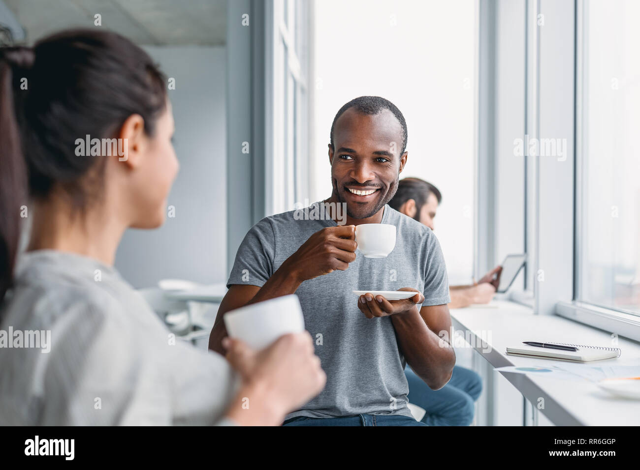 Portrait of multicultural employees dressed in casual wear, laughing while enjoying coffee break during working process in modern office interior, beh Stock Photo