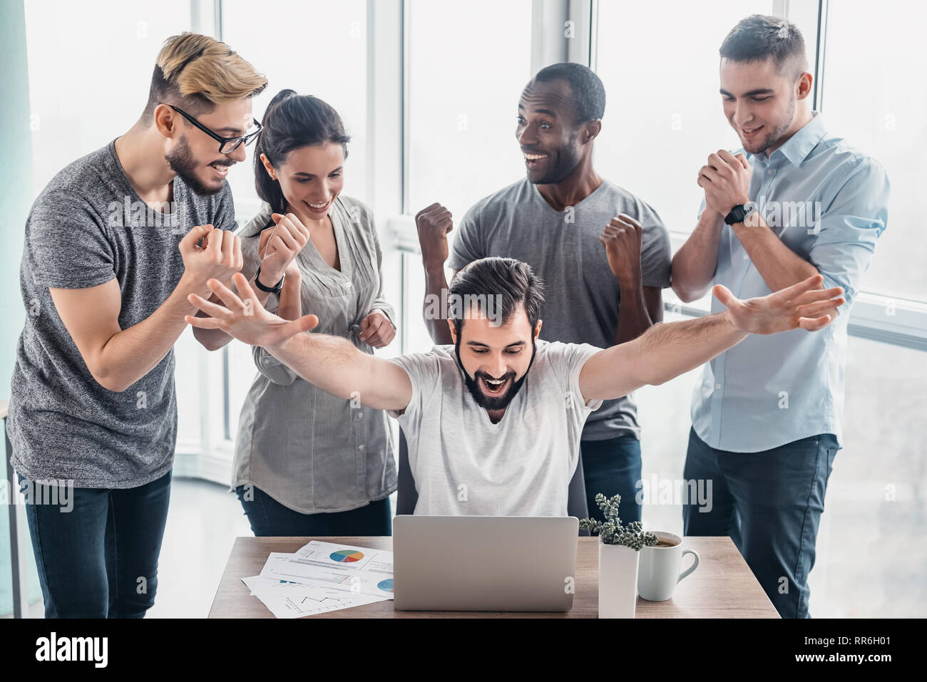 Five diverse business people rejoicing together over a laptop while working in office boardroom. Business team working on their business project together at office. They get a deal. Concept of success Stock Photo