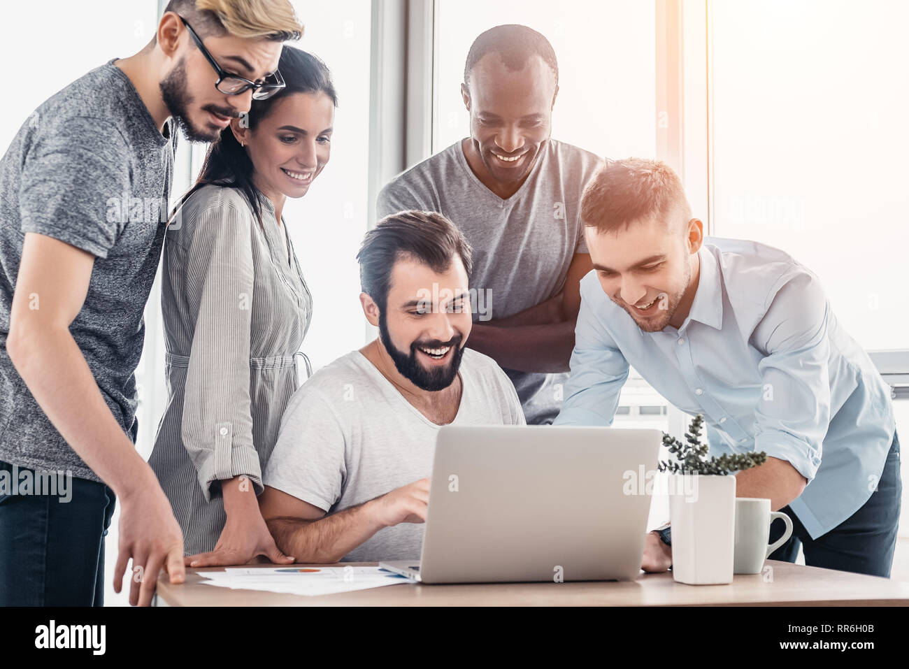 Five diverse business people talking together over a laptop while working at a table in office boardroom. Business team working on their business project together at office. Bright light in the upper right corner Stock Photo