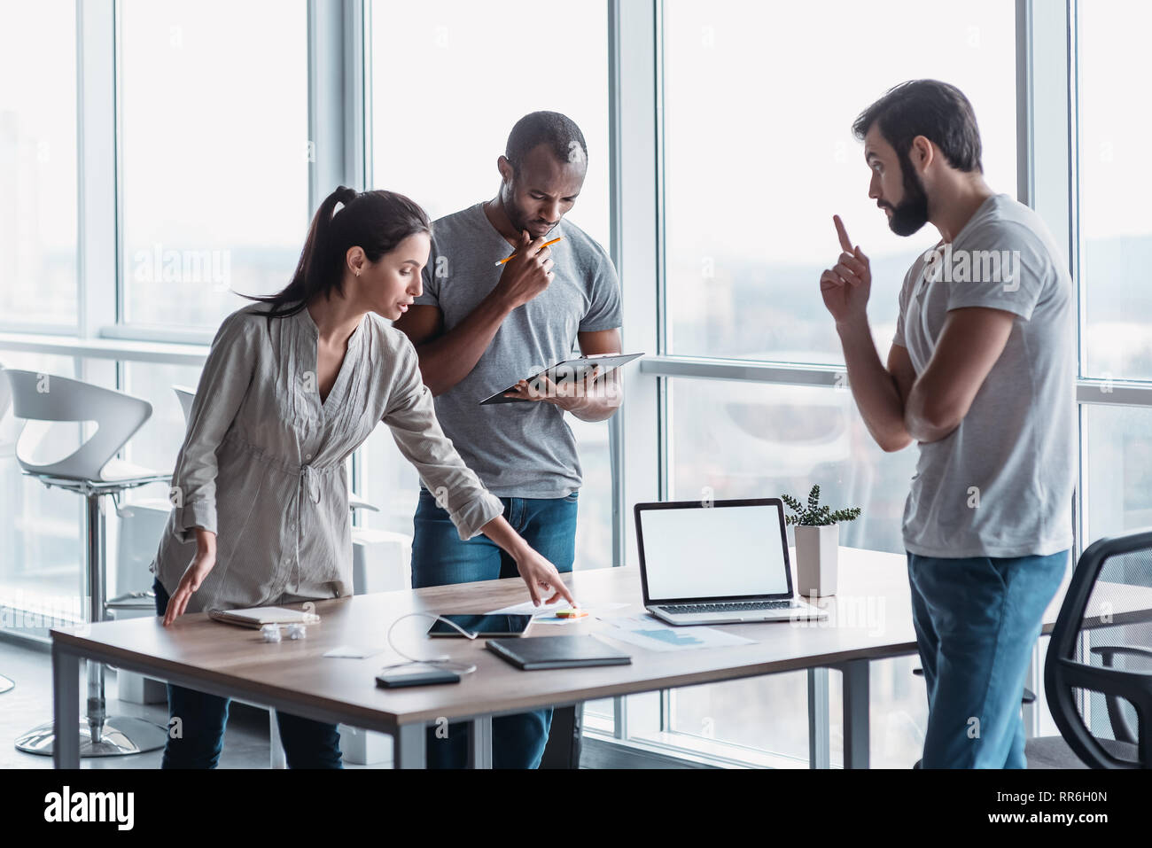 Group of attractive multiracial businesspeople working together in creative office while standing near the wooden desk, friendly multi-ethnic business team discussing business issues at meeting Stock Photo