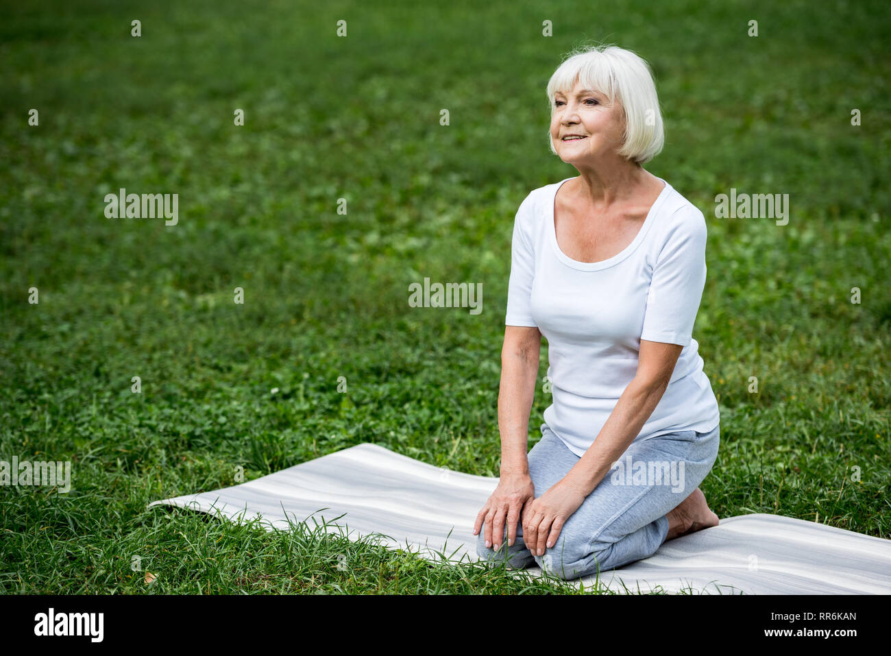 smiling senior woman sitting on yoga mat in meditation pose with hands ...