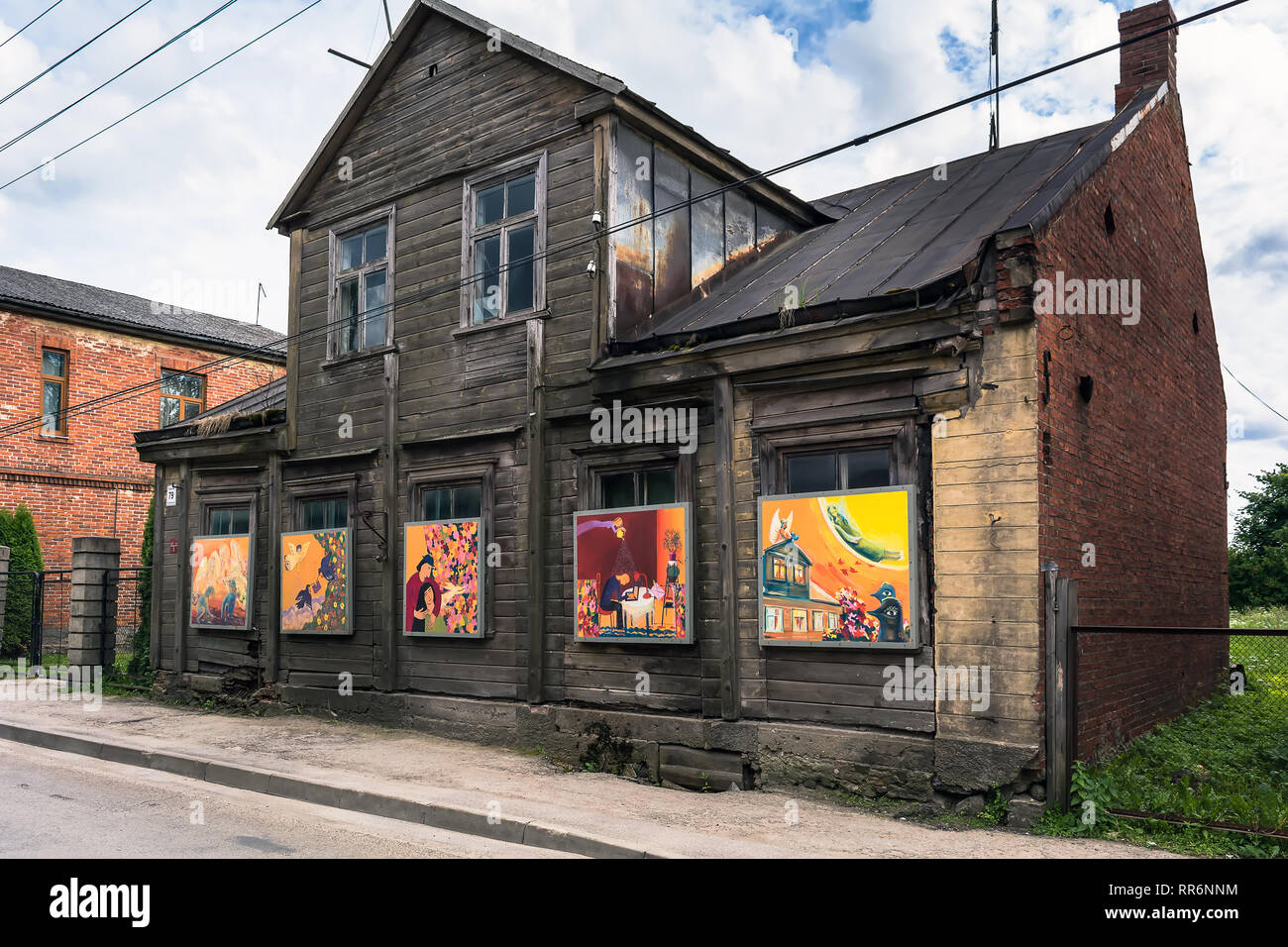 Jekabpils, Latvia - June 25 2017: Old abandoned two-storey sombre wooden building with bright colourful paintings instead of windows. Opposites and co Stock Photo