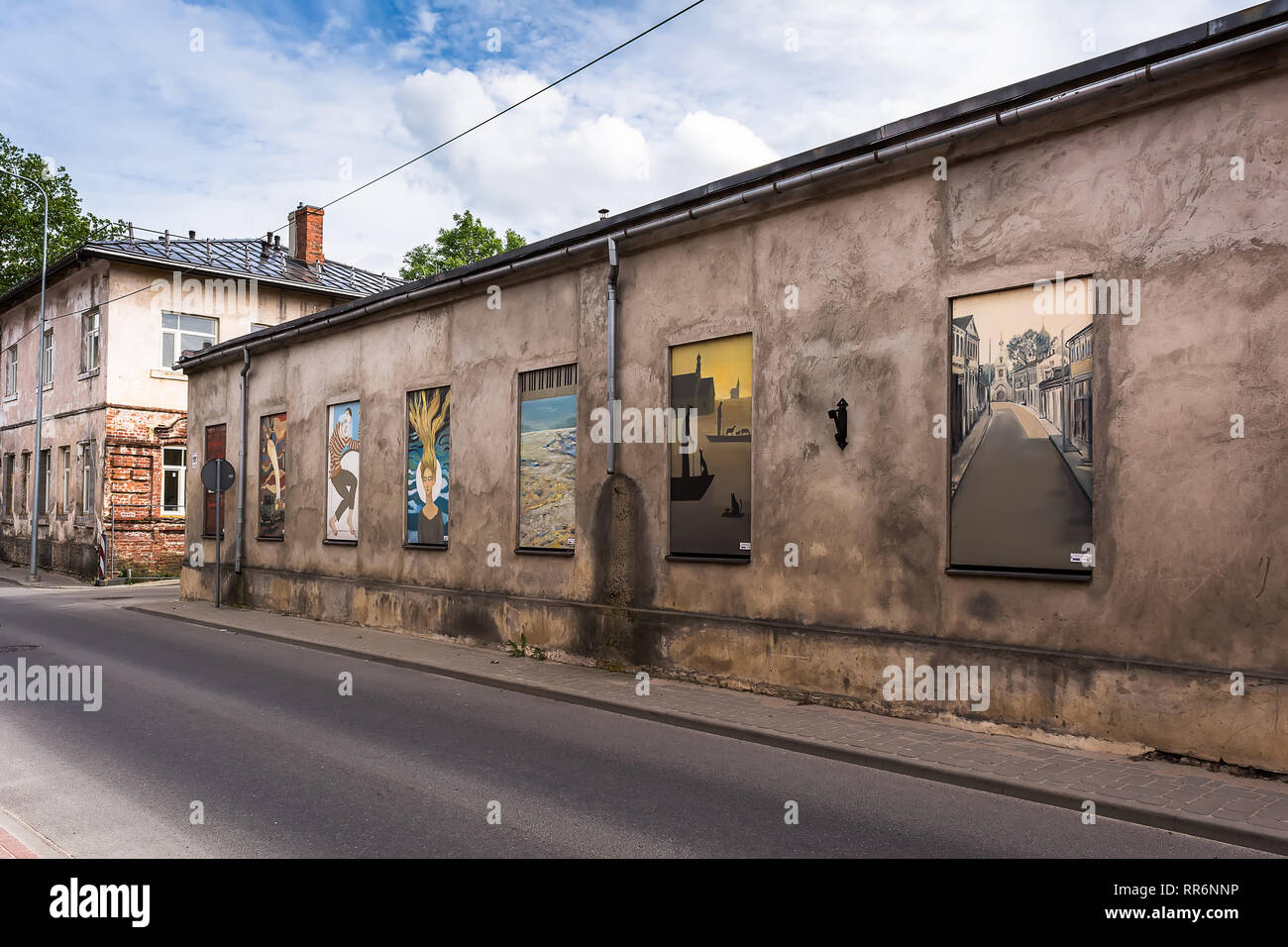 Jekabpils, Latvia - June 25 2017: Old abandoned single-storey sombre stone building with bright colourful paintings instead of windows. Opposites and  Stock Photo