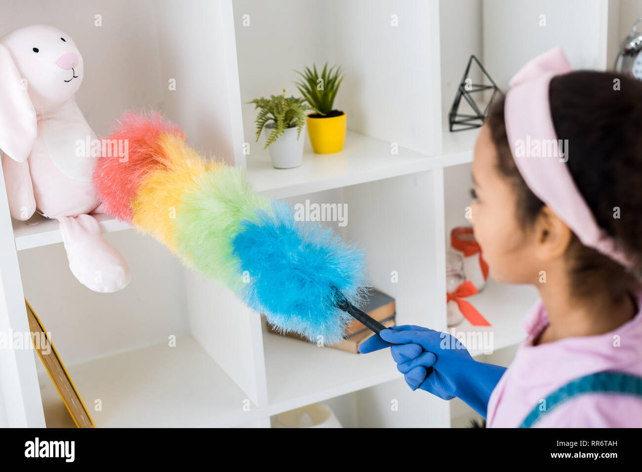 cute african american kid dusting shelving unit with multicolored