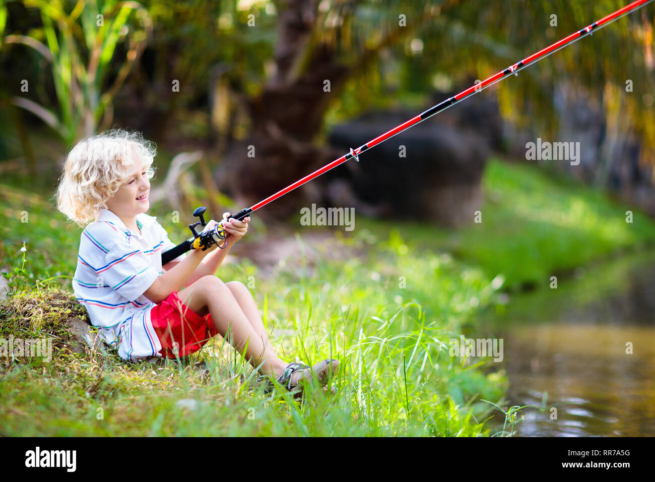 Boy fishing. Child with red rod catching fish in river on sunny summer day.  Outdoor and nature activity for kids. Little boy sitting at lake shore. Ch  Stock Photo - Alamy