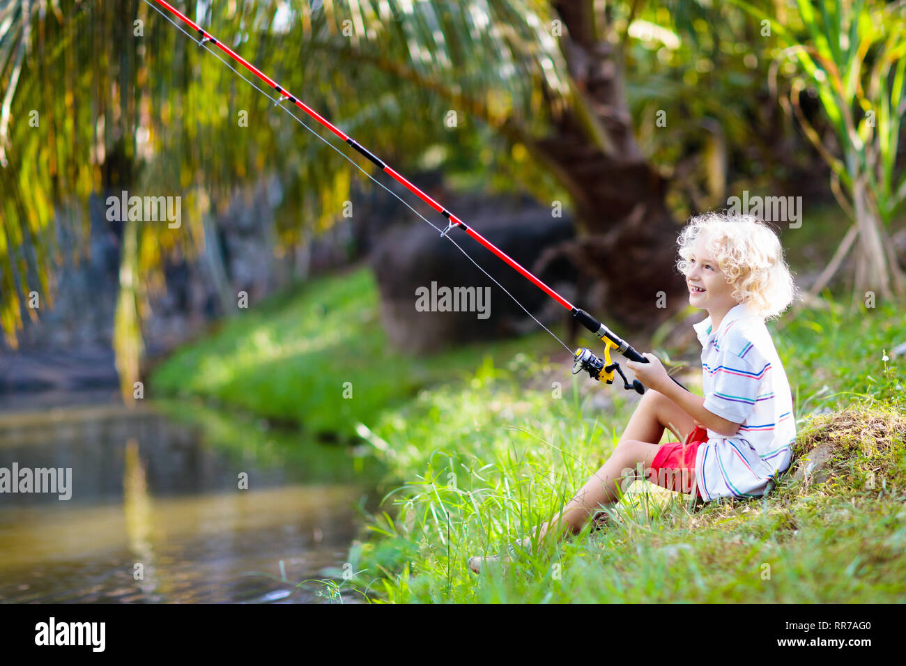 Boy fishing. Child with red rod catching fish in river on sunny summer day.  Outdoor and nature activity for kids. Little boy sitting at lake shore. Ch  Stock Photo - Alamy
