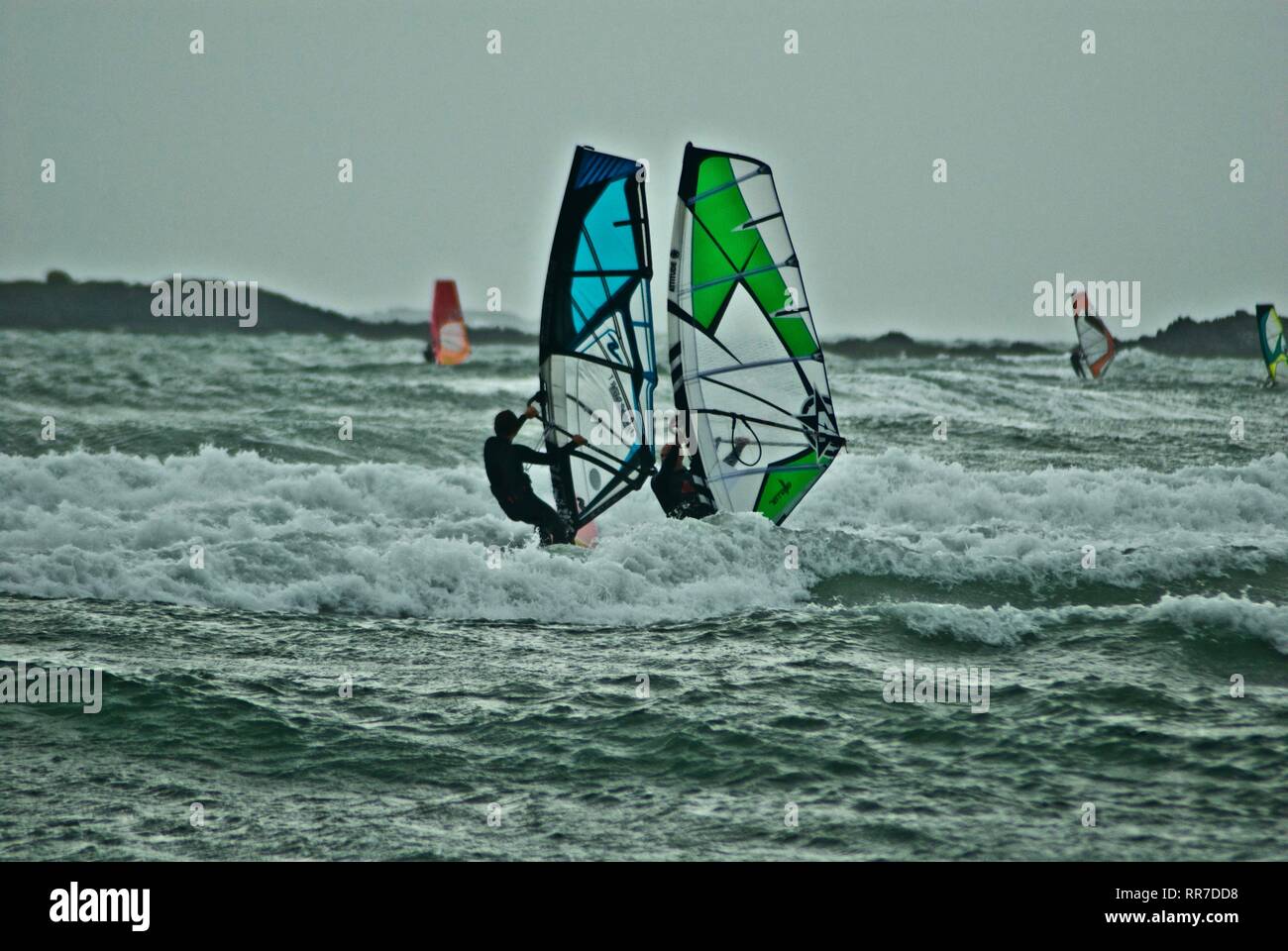 Wind surfers sail on dramatic white water in grey overcast weather in Rhosneigr, Anglesey, North Wales, UK Stock Photo