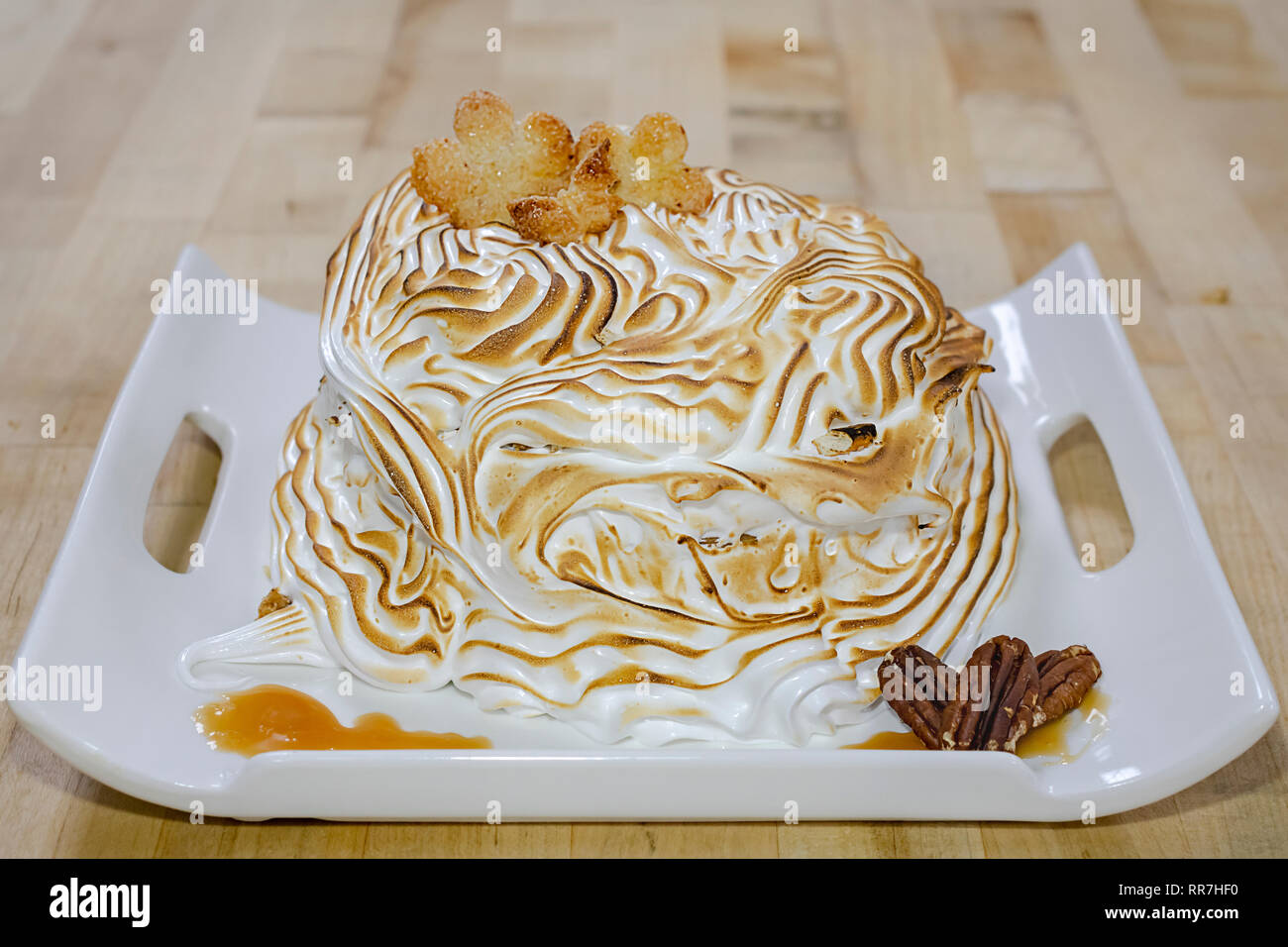 A toasted meringue dessert on a white square plate topped with sugared cookies. Stock Photo