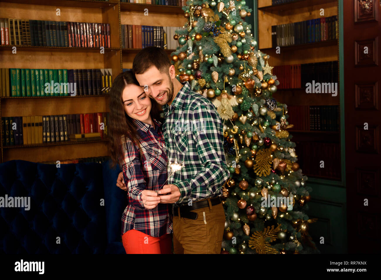 Young beautiful kisser and burning sparklers. Loving couple in Christmas decorated room. Stock Photo