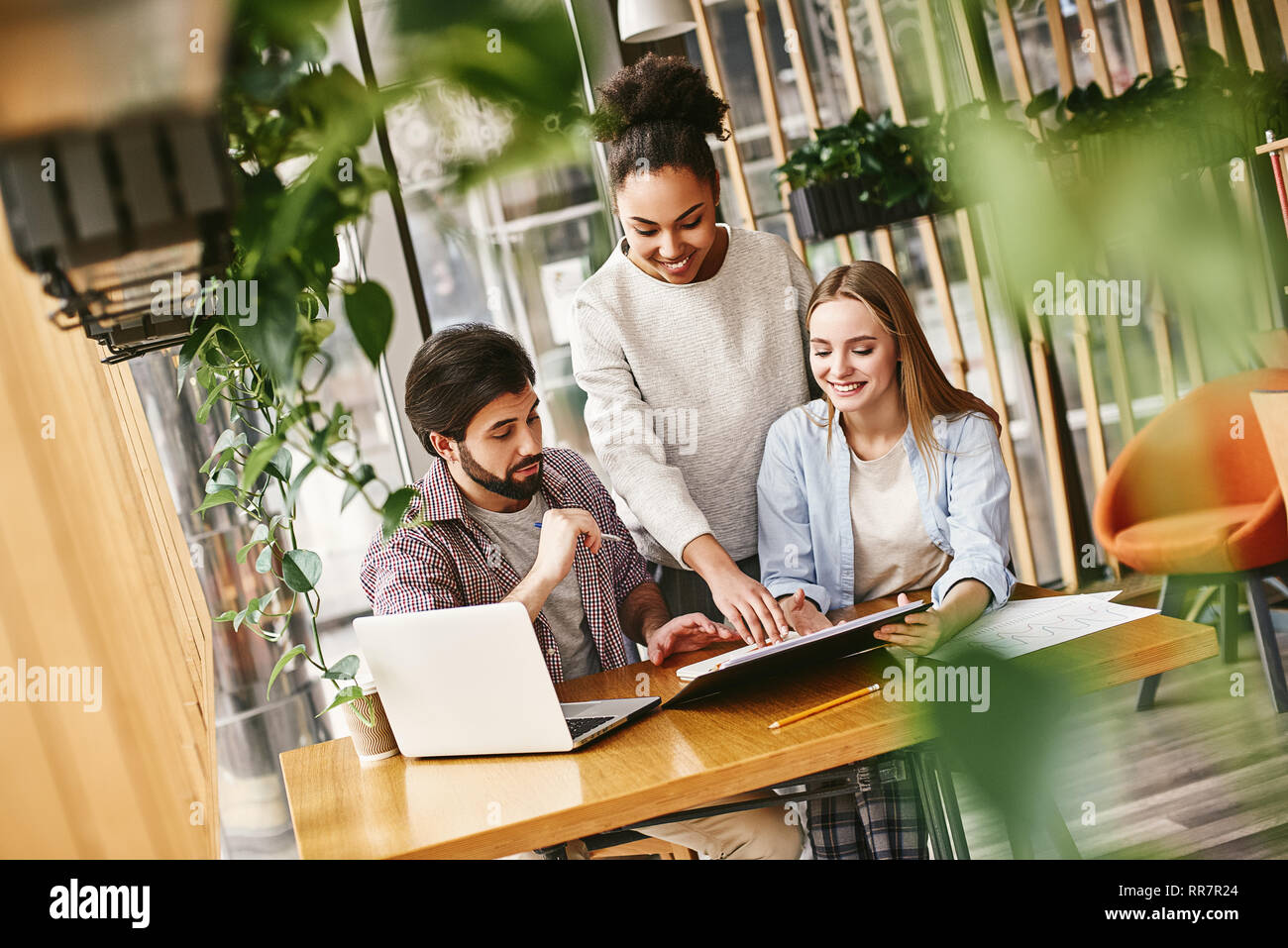 Young woman discussing market research with colleagues on a meeting. Team of young professionals having a meeting in cozy office, looking at their working plan. They are motivated for success. Stock Photo