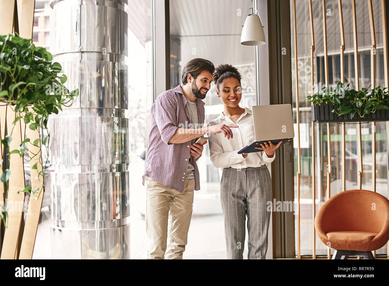 Full-length shot of young business people in smart casual wear concentrating on work while looking at the laptop and smiling. Concept of success Stock Photo