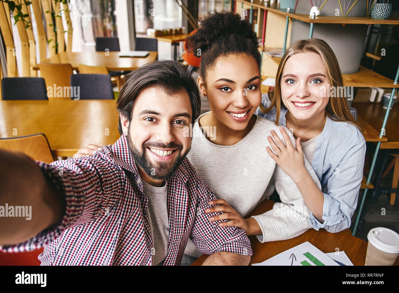 Three laughing young business people in casual wear smile to make shot of themselves. Office interior, bookshelves in the background. Concept of success Stock Photo