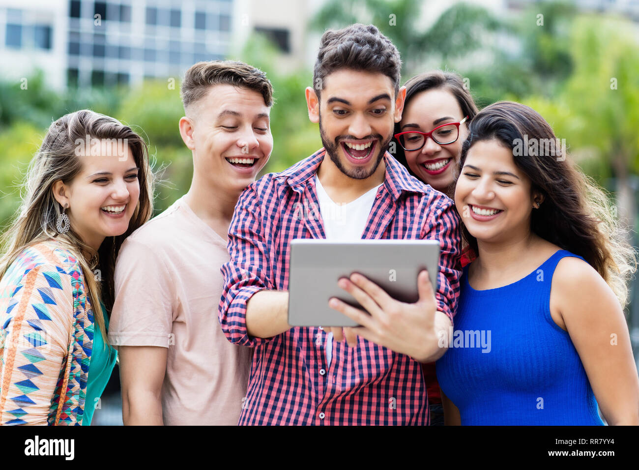 Happy spanish hipster student with tablet computer and group of
