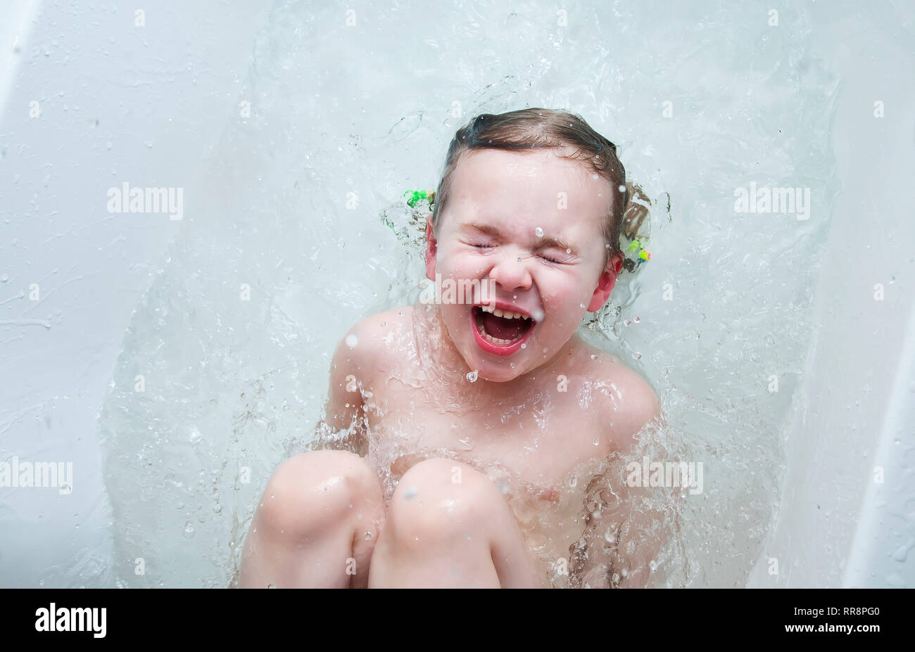 Little baby girl in the bath playing with water drops and splashes