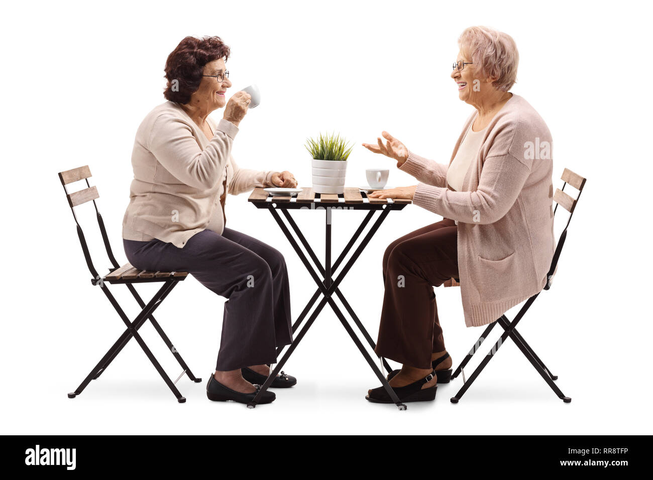Full length profile shot of two elderly women drinking coffee at a table and talking isolated on white background Stock Photo
