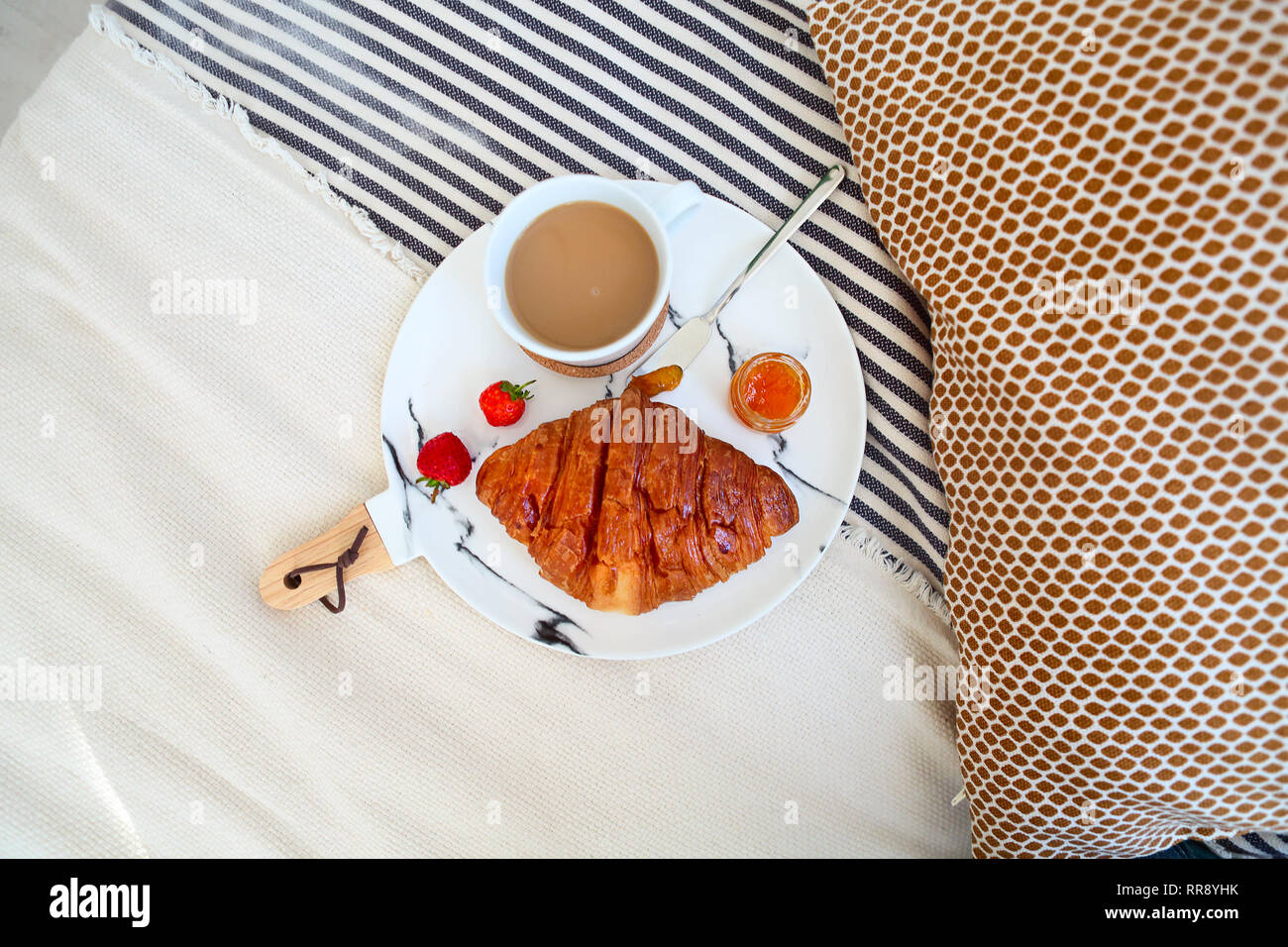 Breakfast with croissant, coffee, strawberry and jam on the plate tray in bed. Top view Stock Photo