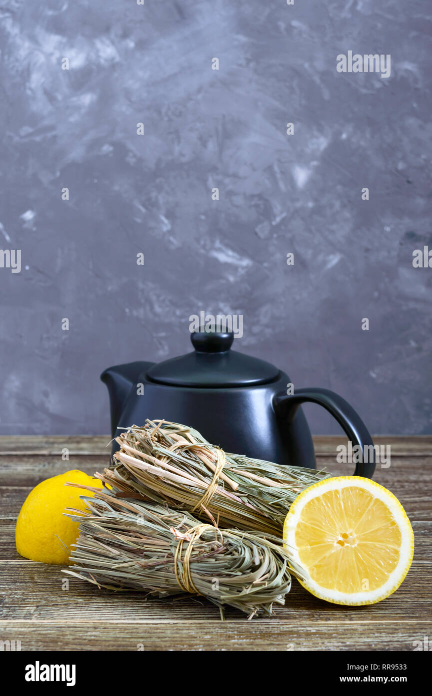 Organic dry lemongrass (Cymbopogon flexuosus) in bunches and lemon fruit on a wooden table. Herbs for tea. Stock Photo