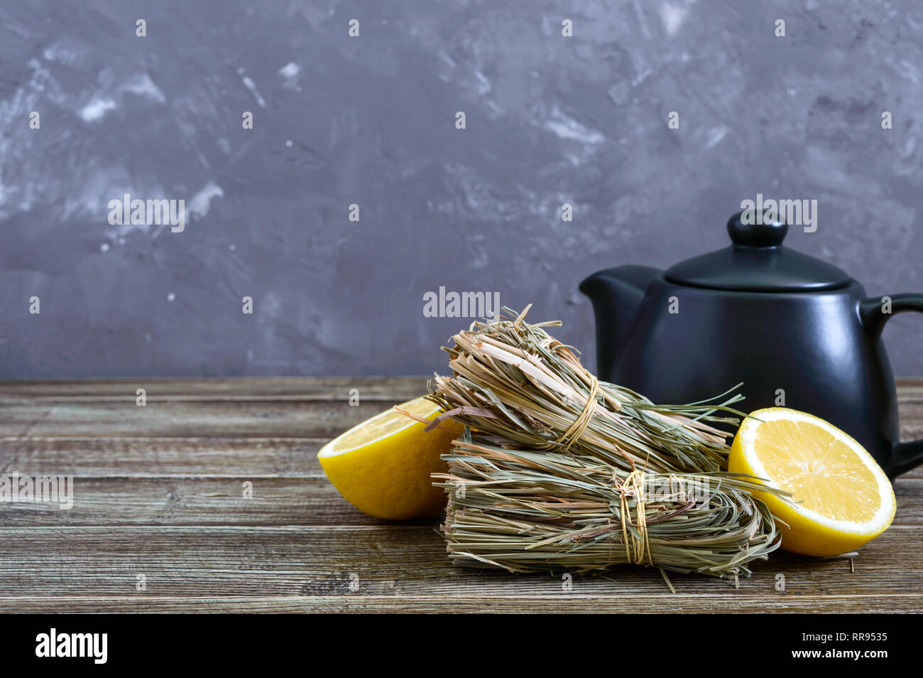 Organic dry lemongrass (Cymbopogon flexuosus) in bunches and lemon fruit on a wooden table. Herbs for tea. Stock Photo