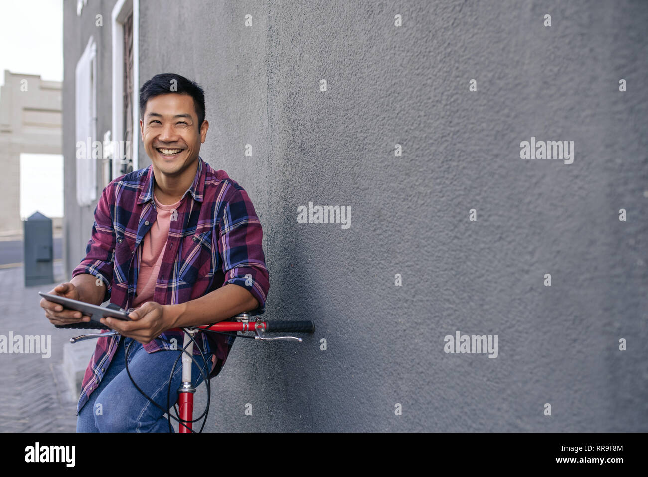 Smiling young man leaning on his bicycle using a tablet Stock Photo
