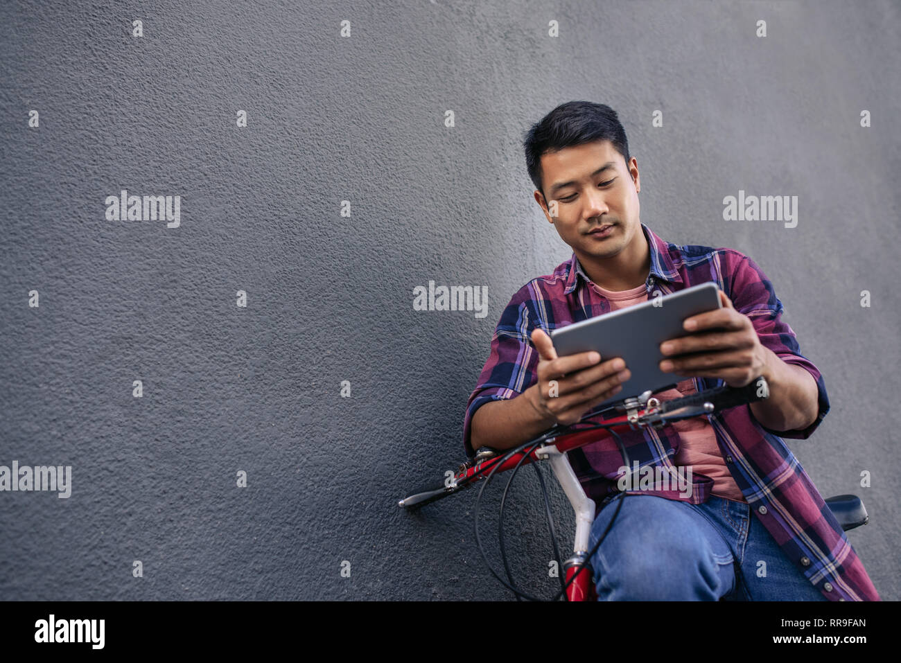 Young man leaning on his bicycle using a tablet Stock Photo