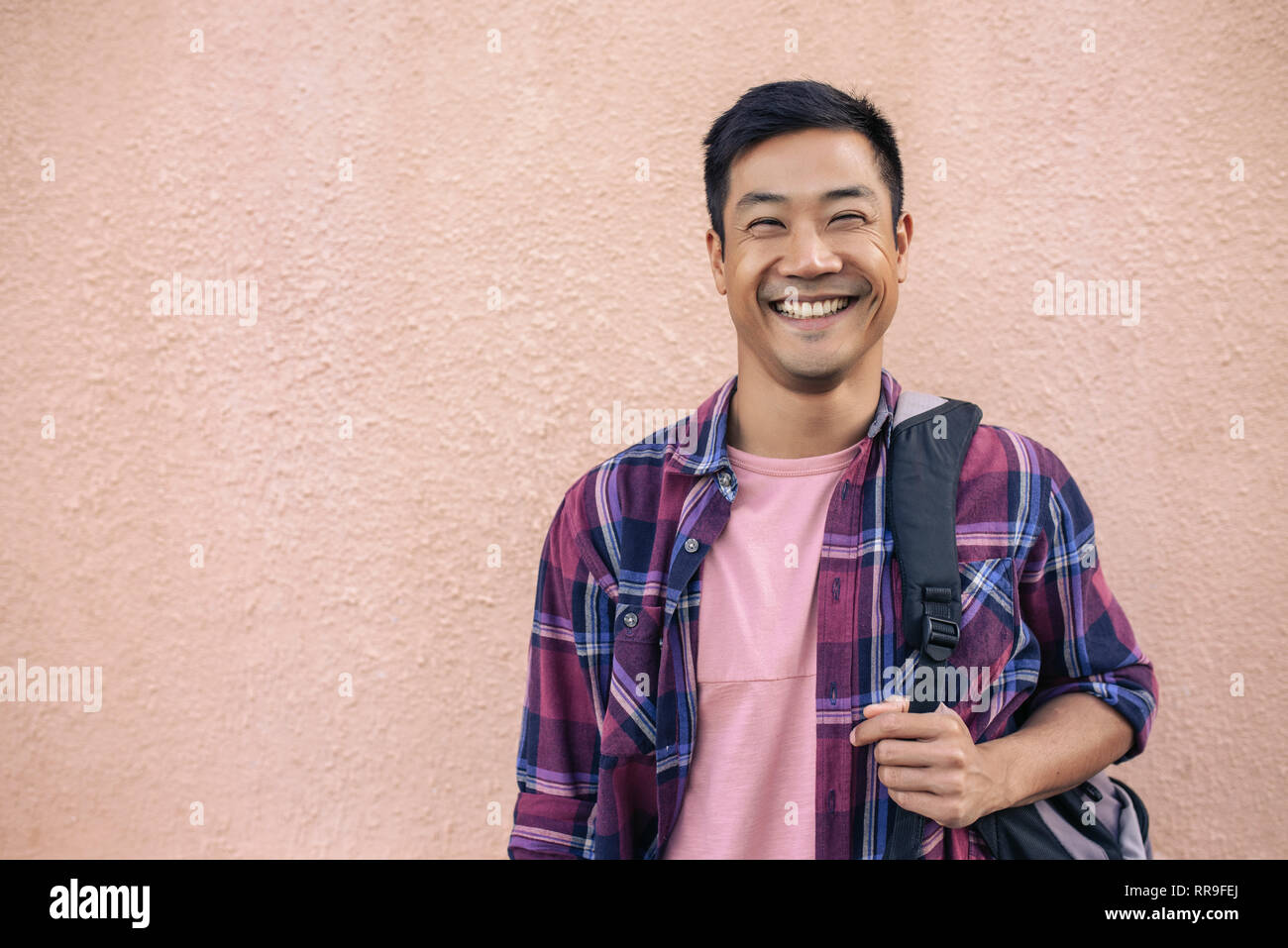 Smiling young man standing outside carrying a backpack Stock Photo