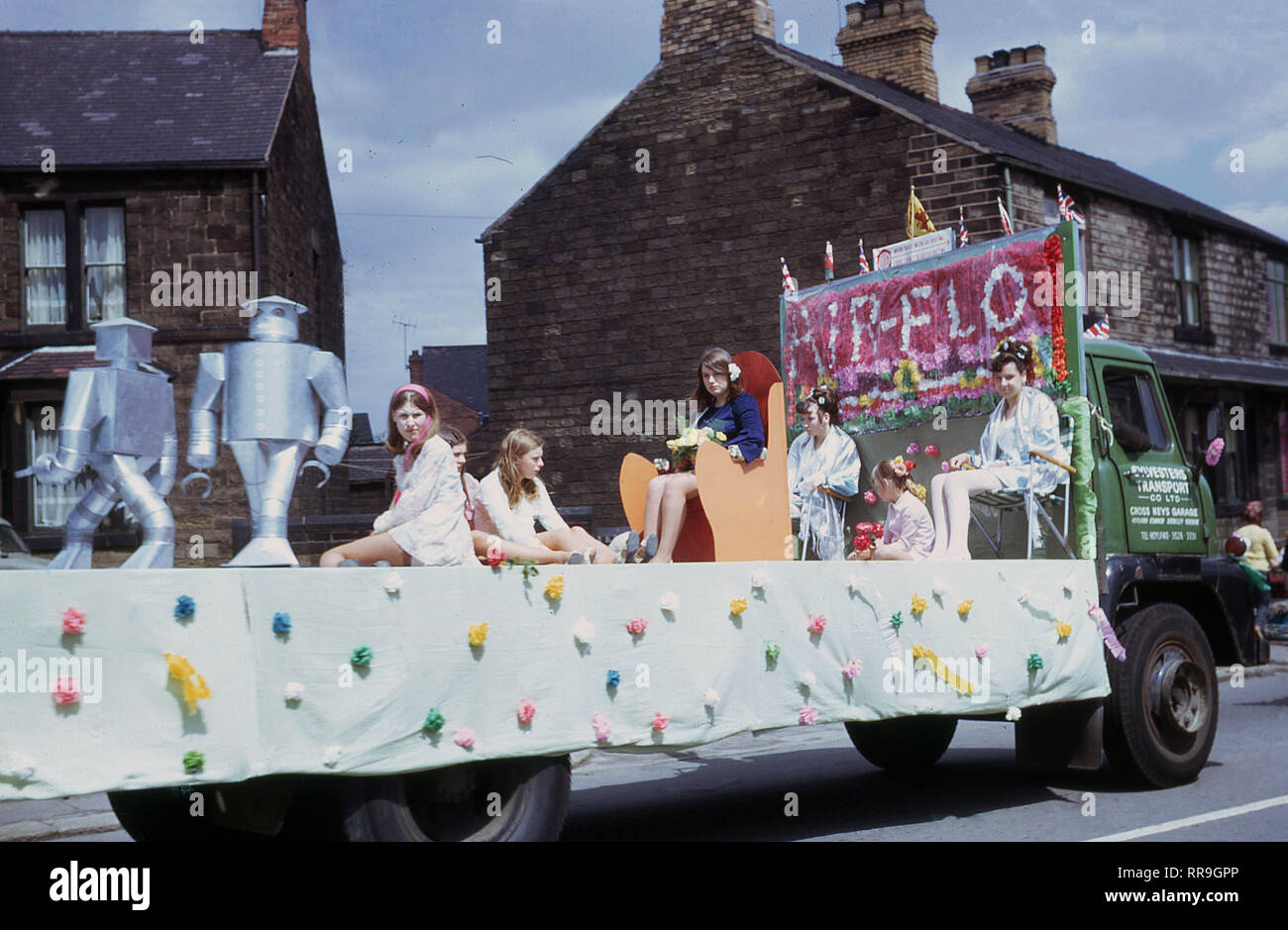 1960s, historical, travelling in a carnival through a northern village, England, UK. we see ladies and girls sitting on a decorated float - sponsored by 'Air-Flo' - on the back of an open Slyvesters Transport truck. Air-Flo was founded in the USA in the 1940s by three brothers looking for a better way to harvest onions and subsquently became leading manufacturers of harvesting equipment. Stock Photo