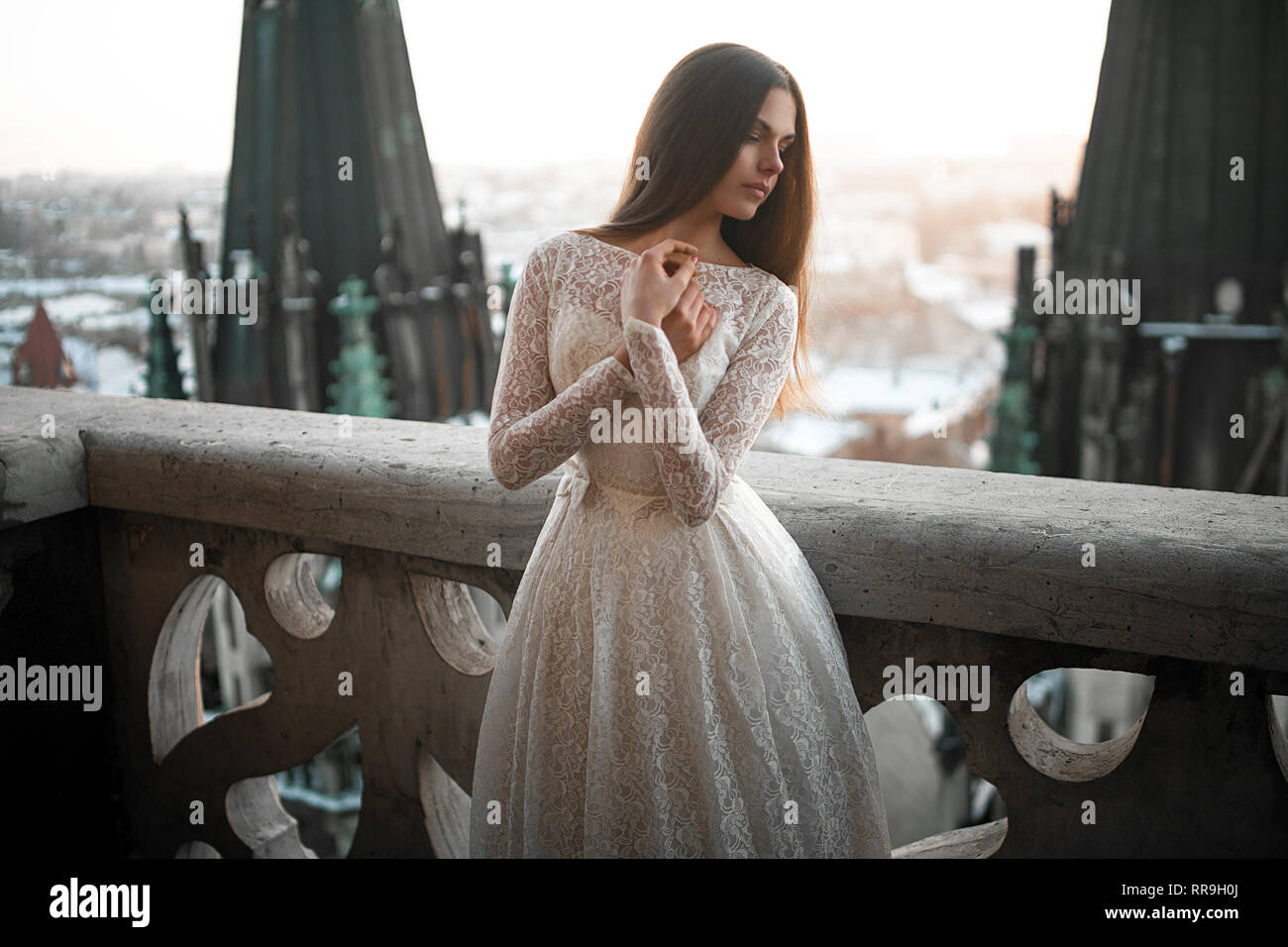 Beautiful young woman stands in white lacy dress on the balcony against