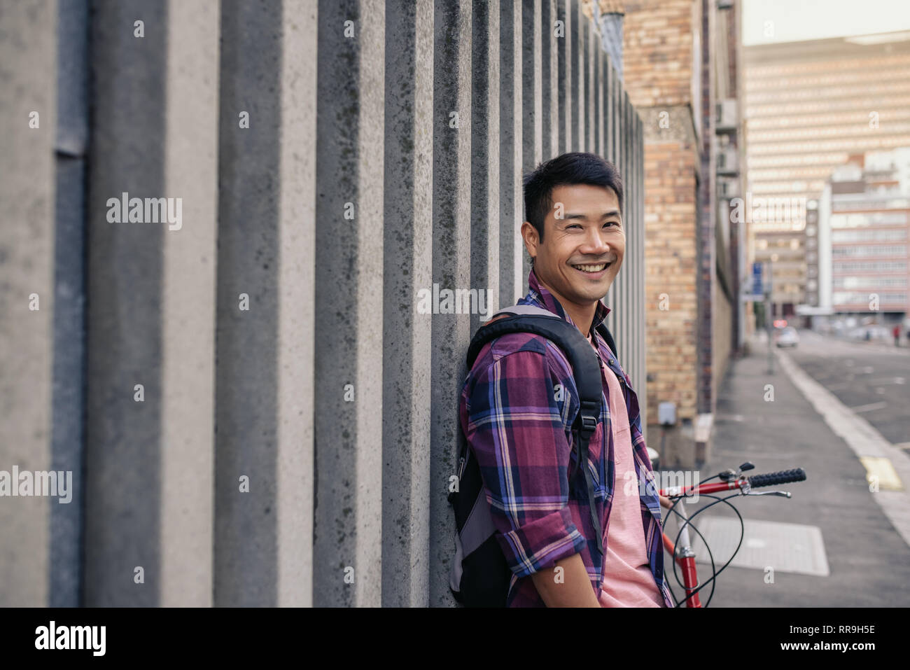 Smiling young man leaning against a wall with his bicycle Stock Photo ...