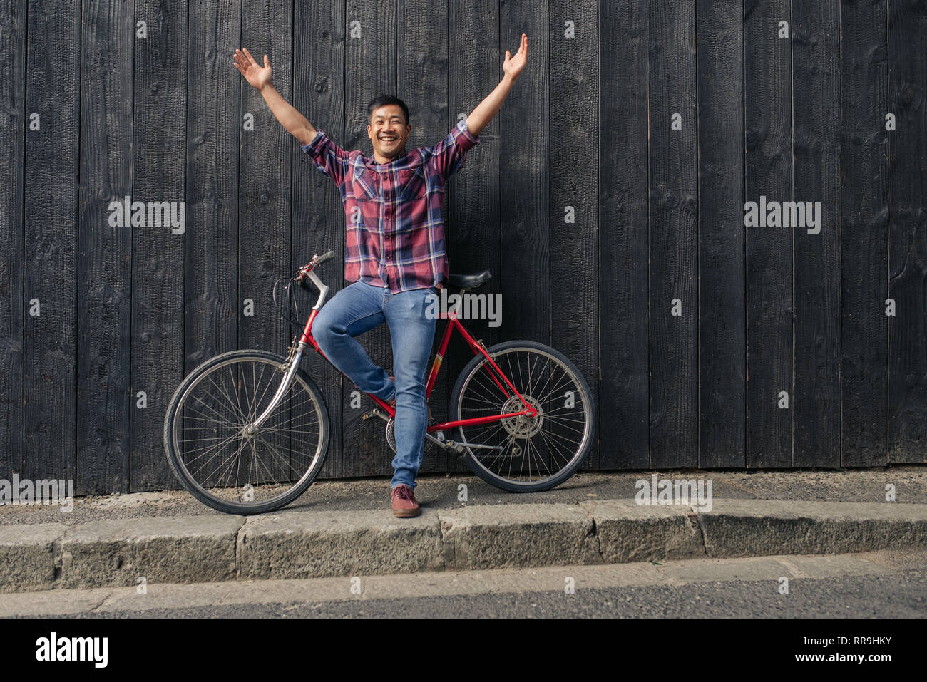 Smiling young man with a bike raising his arms skyward Stock Photo