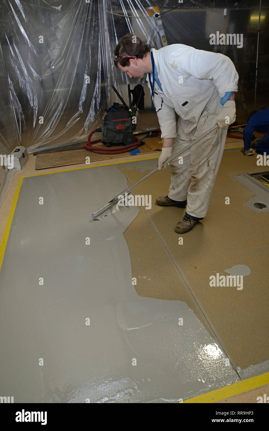A tradesman spreads an epoxy flooring product in an industrial building. The plastic curtain keeps the job from becoming contaminated. Stock Photo