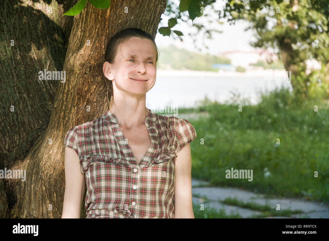 Portrait of a beautiful mature caucasian woman under an elm tree close to the river during a sunny winter day Stock Photo