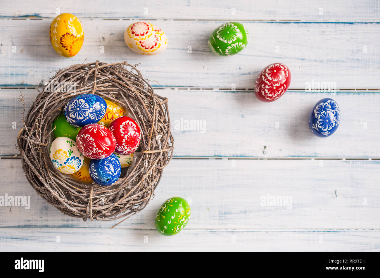 Close-up multicolored easter eggs in basket on wooden table. Stock Photo