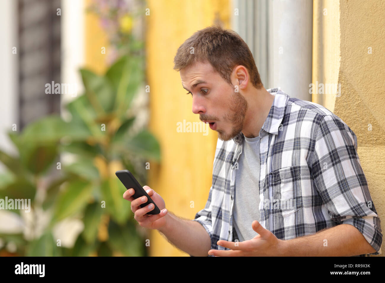Surprised man using smart phone finding amazing content standing in a colorful street Stock Photo