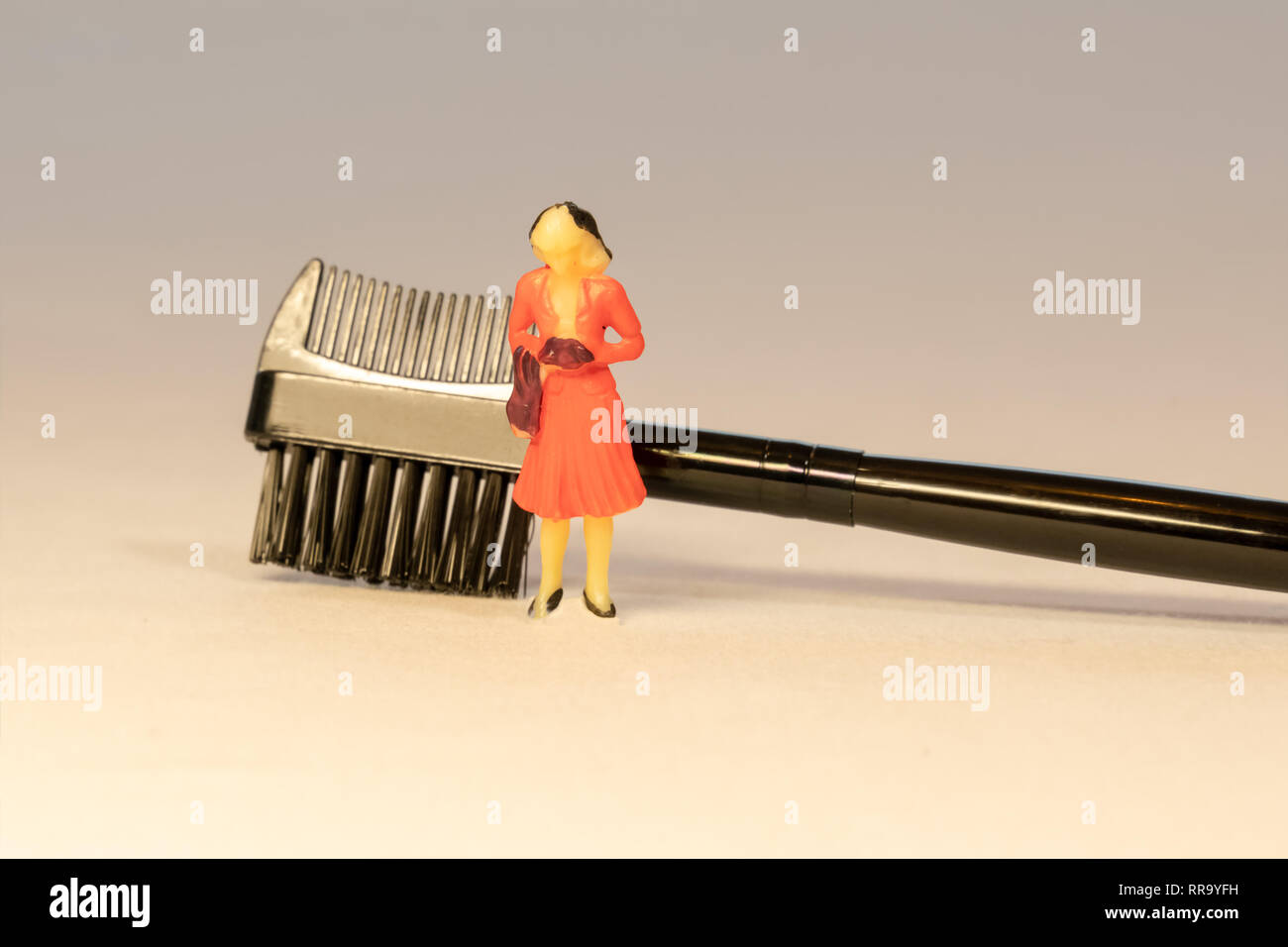 Miniature woman in orange dress next to black brow lash groomer brush. Beauty and Skin care concept. Stock Photo