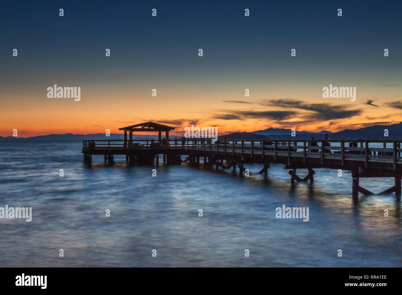 Watching the sun set behind the wooden pier at Davis Bay, Sechelt on the Sunshine coast Stock Photo