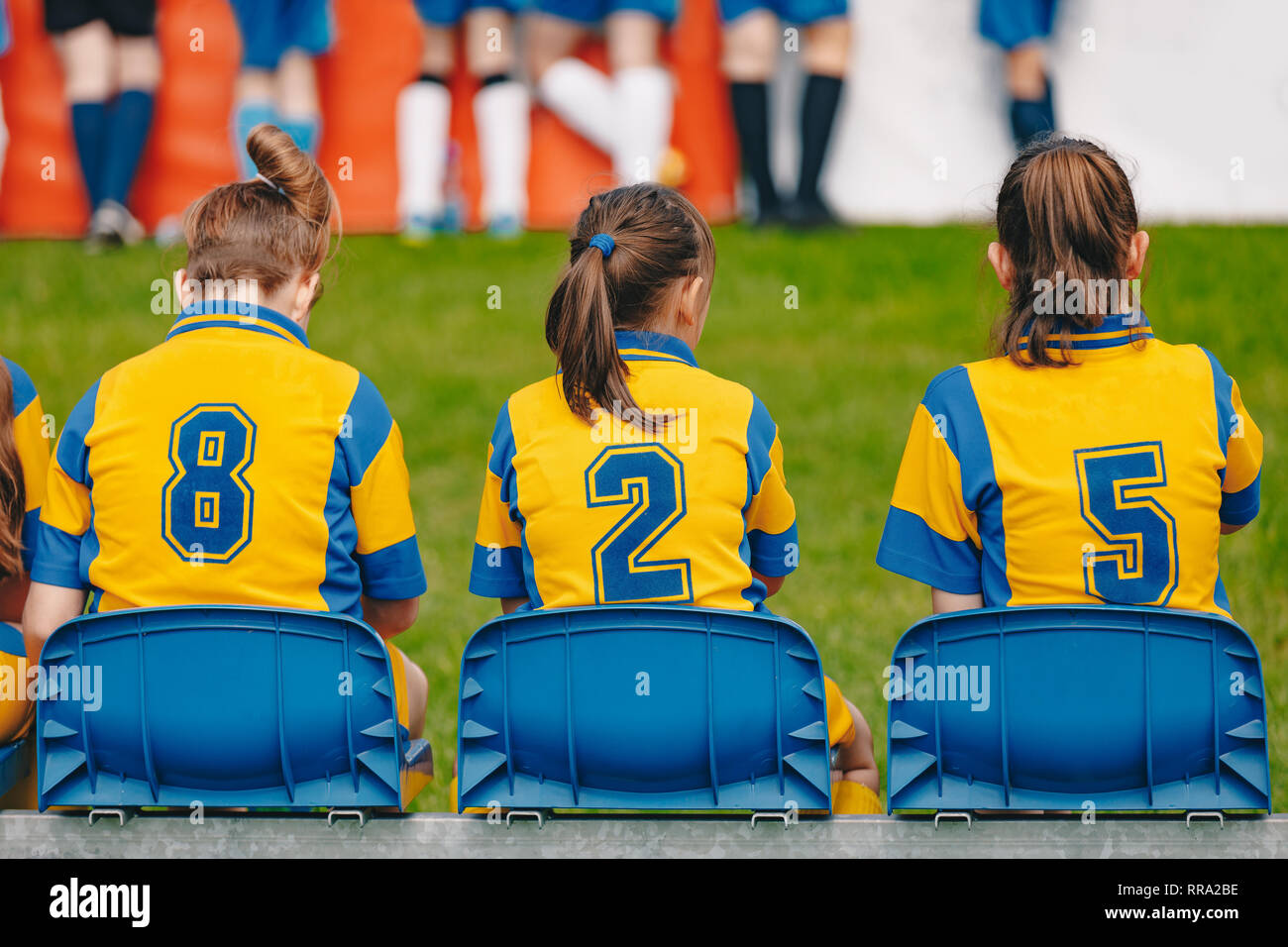 Kids girls elementary school sports team sitting on bench on the grass field. Soccer football junior girls team at sports outdoor field before match Stock Photo