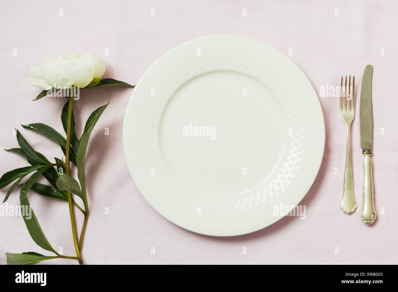 Spring romantic dinner. Elegance table setting peony flowers on tablecloth. Top view. Stock Photo