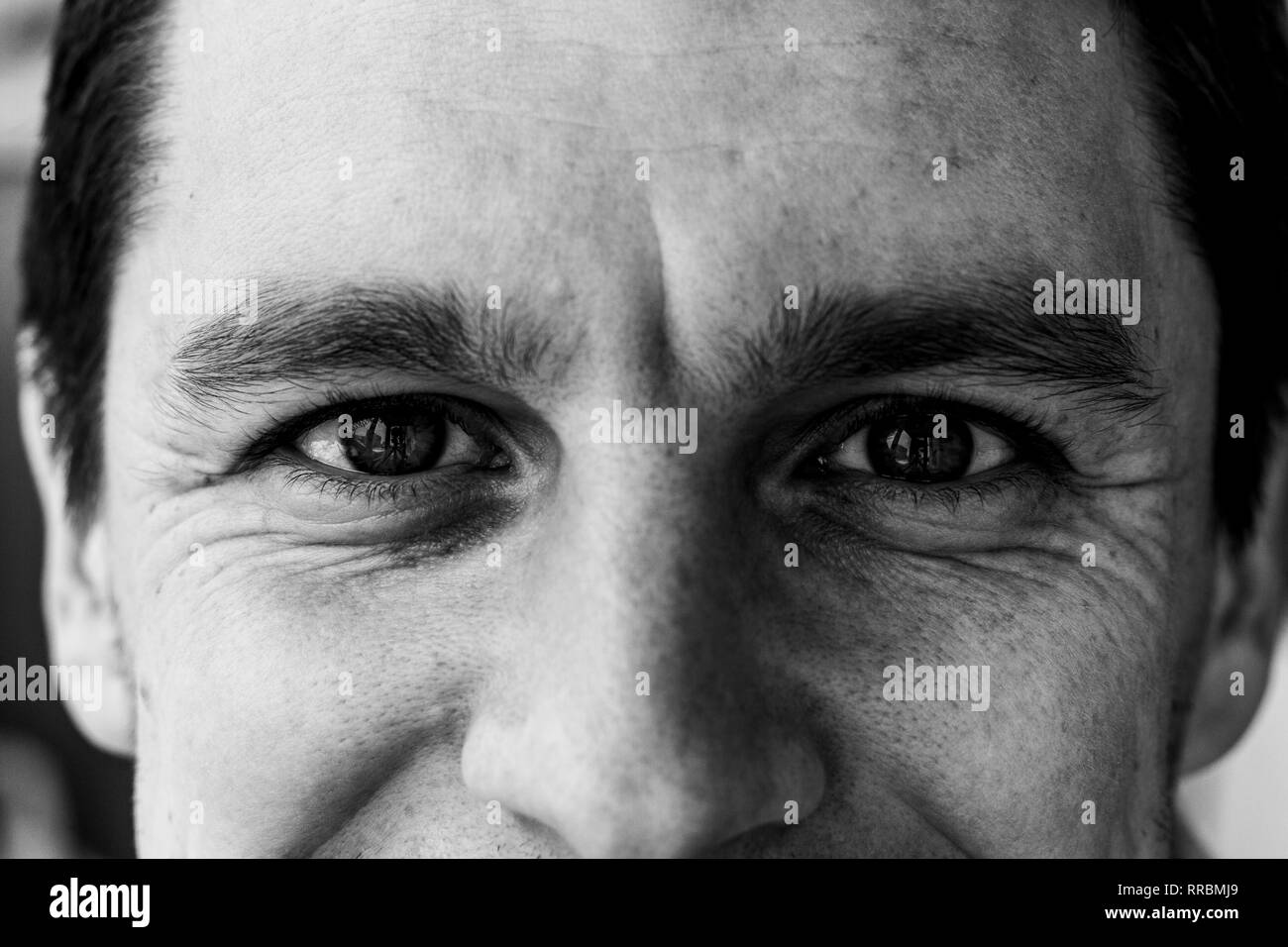 Fragment of a man's face: an eyes and nose to compile an identikit. Fragment of the wrinkled face of a young guy. Smiling eyes of a man. Black and whi Stock Photo