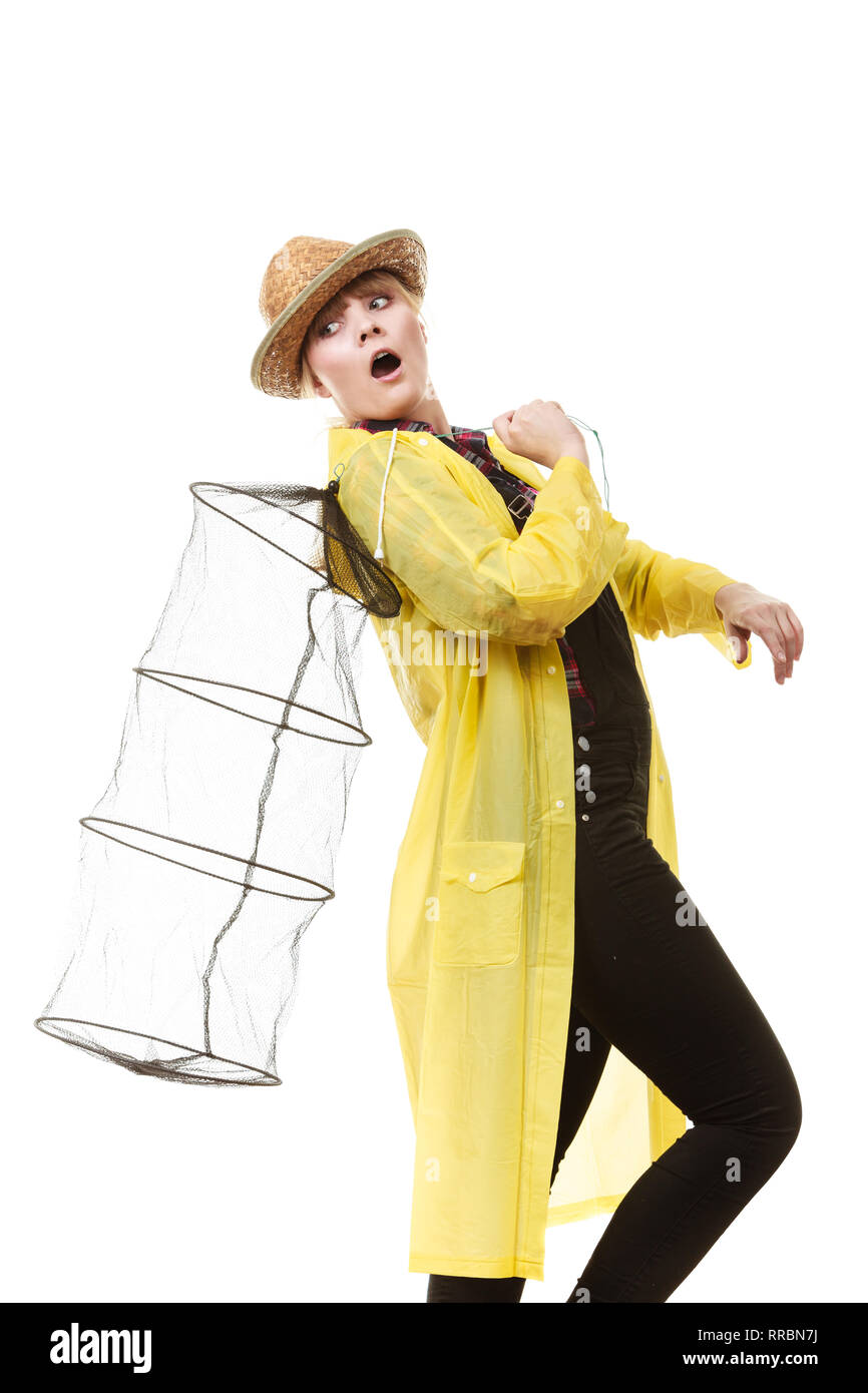 Spinning, angling, cheerful fisherwoman concept. Happy woman in yellow raincoat holding empty fishing keepnet, having fun. Stock Photo