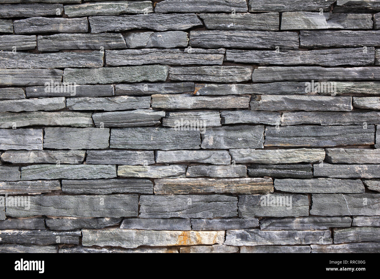Grey stone granite wall made of stacked pieces stones. Full frame image