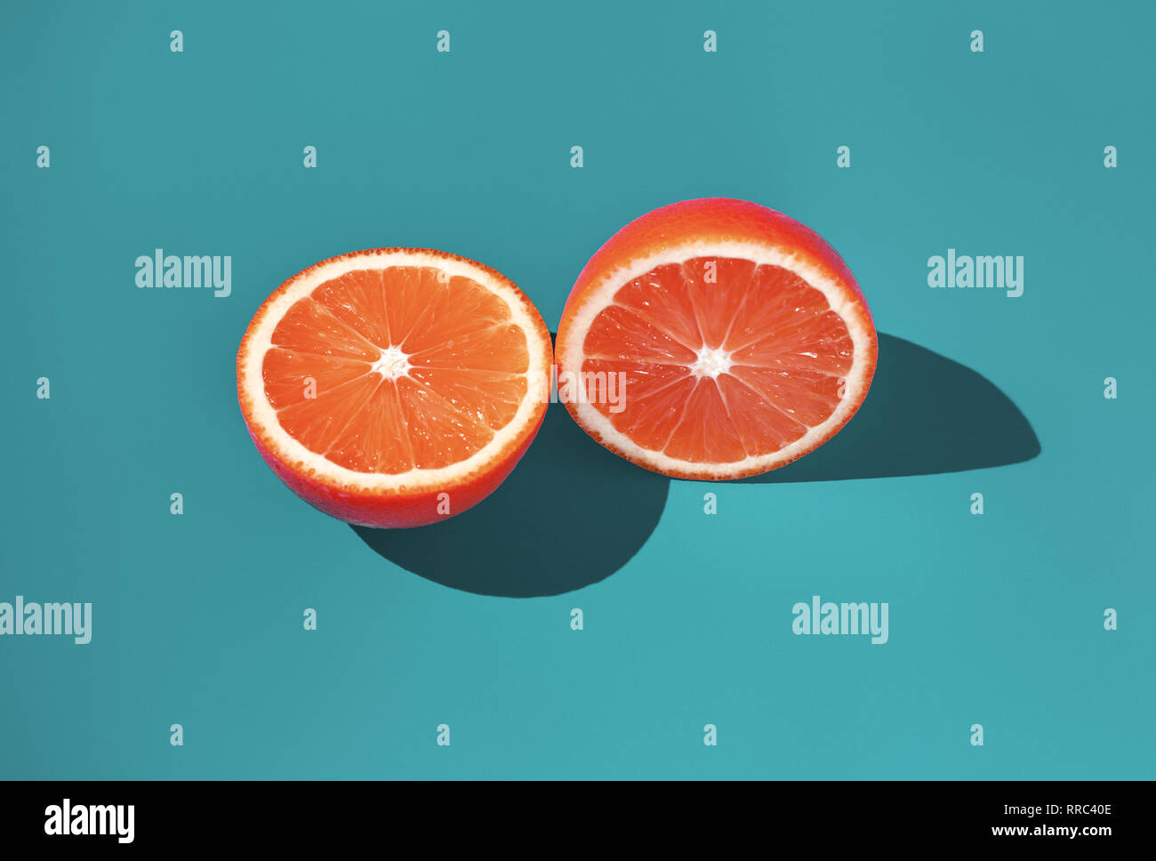 Two halves of ripe orange on a green background in bright sunlight Stock Photo