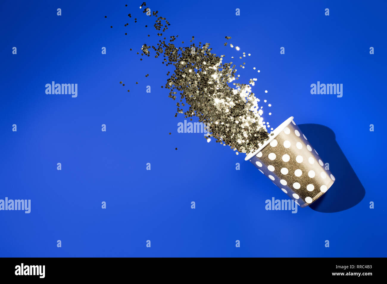 Golden paper cup for birthday party with golden confetti on blue background Stock Photo